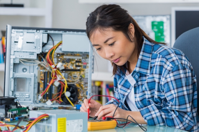 A technician works on an open computer tower, using electronic testing tools surrounded by cables and components.